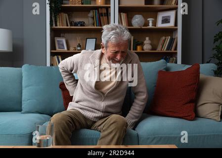 L'homme âgé à cheveux gris âgé à visage rouge âgé se wirthes dans la douleur souffre de la faible tension du dos, le frottement au toucher ou le massage de la longe réduit le mal de dos. Disque dégénératif Banque D'Images