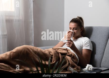 Grippe. Femme attrapée par le froid. Éternuer dans les tissus. Maux de tête. La médecine du virus. Jeune femme infectée par le froid soufflant son nez à Handkerchief. Femme malade W Banque D'Images