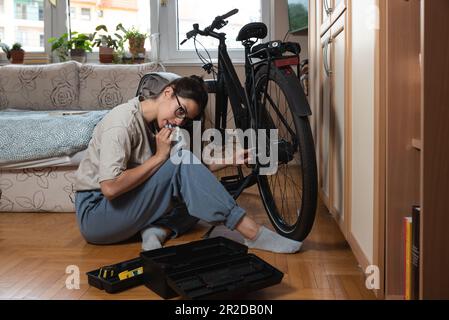 Jeune femme ou jeune mécanicien autodidacte qui fixe et répare sa bicyclette à sa maison. Chaîne de réparation femelle sur la roue arrière avant qu'elle commence à rouler Banque D'Images