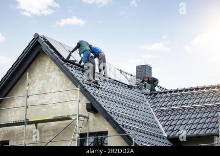 Travailleurs installant des panneaux solaires sur le toit d'une maison unifamiliale allemande Banque D'Images