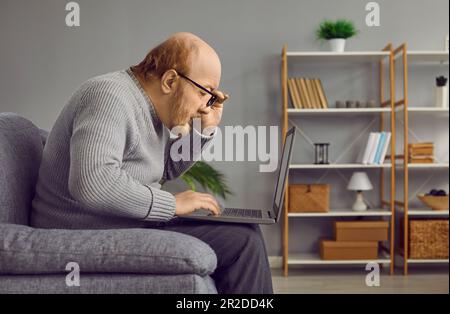 Homme âgé touchant le rebord de ses lunettes en regardant attentivement l'ordinateur portable Banque D'Images