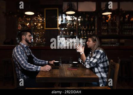 Les hipsters millénaires mari et femme propriétaires de café bar restaurant assis dans la soirée après la clôture de parler de vérification des bénéfices, ventes calcul ORD Banque D'Images