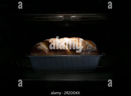 Un pain de ferme blanc dans un moule à pâtisserie dans un four électrique juste en haut éclairé par la lumière du four Banque D'Images