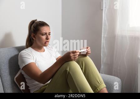 La jeune femme nerveuse est assise à la maison pour un test de grossesse et attend impatiemment le résultat du test. Peut-être enceinte peut-être pas concept avec Banque D'Images