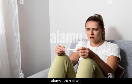 La jeune femme nerveuse est assise à la maison pour un test de grossesse et attend impatiemment le résultat du test. Peut-être enceinte peut-être pas concept avec Banque D'Images