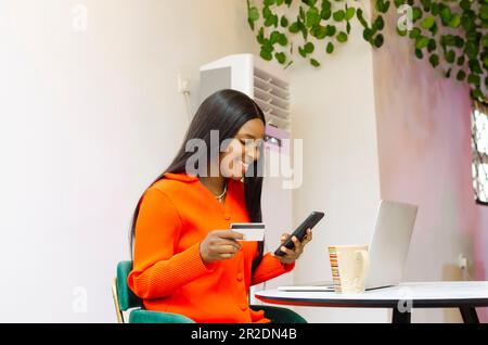 Une femme de bureau noire attrayante magasinent en ligne avec un smartphone et une carte de crédit à portée de main Banque D'Images