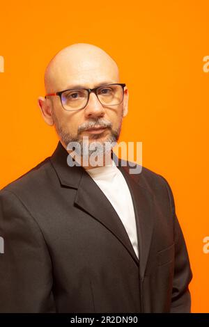 Homme élégant dans une veste de costume, barbu, chauve et portant des lunettes. Isolé sur fond orange Banque D'Images