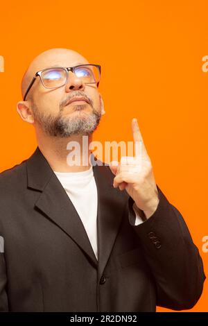 Homme élégant dans une veste de costume, barbu, chauve et portant des lunettes. Isolé sur fond orange Banque D'Images