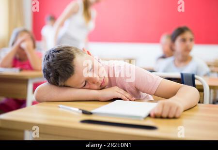 Garçon d'école fatigué dormant en classe pendant la leçon Banque D'Images