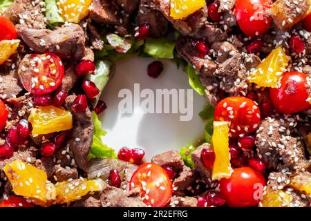 Salade chaude avec foie de poulet, tomates cerises, orange, laitue, graines de grenade et sésame. Vue de dessus. Gros plan avec mise au point douce sélective Banque D'Images