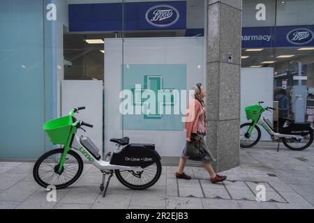 Londres, Royaume-Uni. 19 Mai 2023 Une promenade piétonne passé Lime Location de vélos électriques abandonnés à l'extérieur d'un magasin de pharmacie Boots dans la rue Victoria.compagnies de location de cycle électrique telles que Lime by Uber, Human Forest, et dott, n'ont pas de places de stationnement contrairement à Santander. Le Conseil de Westminster élabore des plans pour les cavaliers qui ne parcoutent pas correctement leurs cycles loués laissés sur des trottoirs qui peuvent poser une obstruction aux piétons et aux utilisateurs de fauteuils roulants. Credit: amer ghazzal / Alamy Live News Banque D'Images