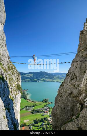 Une femme marche sur la via ferrata au-dessus du pont suspendu, via ferrata Drachenwand, Mondsee en arrière-plan, Drachenwand, Mondsee, Salzkammergut, Salzbourg, Banque D'Images