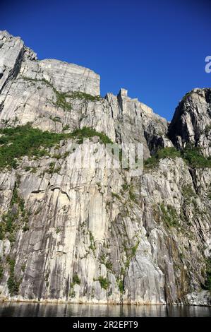 Preikestolen (rocher de Pulpit). 604 mètres / 1982 pieds au-dessus de Lysefjord. Les gens peuvent être vus assis sur le bord du toit plat de 25m x 25m. Banque D'Images