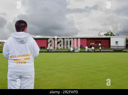 Une femme portant un sweat à capuche blanc joue des boules devant le pavillon rouge du club-House au terrain de bowling de la pelouse de Balornock à Glasgow, en Écosse, au Royaume-Uni Banque D'Images