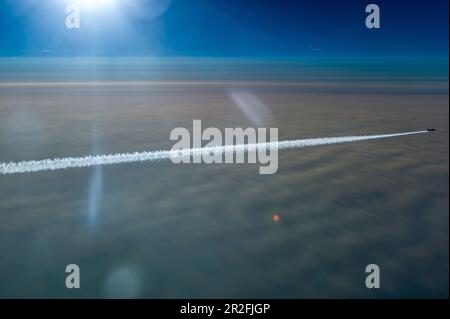 Avion avec contrails sur couverture de nuage fermée dans le rétroéclairage Banque D'Images