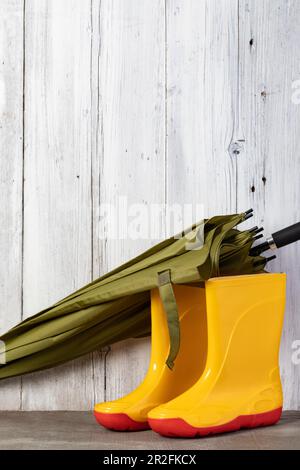 parapluie vert et bottes de gommer contre un mur en bois Banque D'Images