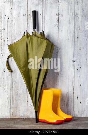 parapluie vert et bottes de gommer contre un mur en bois Banque D'Images