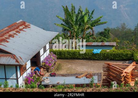 Sikkim, Inde - 22nd mars 2004 : vue de face d'une maison dans le village de Sikkim, une jeune femme sikkimese qui polissage ses ongles de pied. Femmes de Sikkim. Banque D'Images