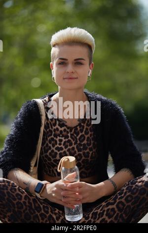 Portrait d'une femme élégante et diversifiée aux cheveux courts. Jeune femme tendance portant des vêtements à imprimé léopard et tenant une bouteille d'eau en verre dans les mains wh Banque D'Images