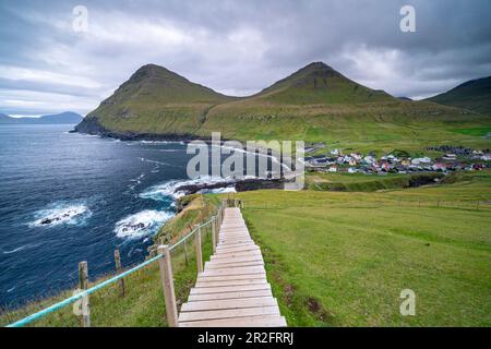 Vue de la côte escarpée à la mer. Un escalier en bois facilite la montée sur la pente raide au-dessus de Gjógv, îles Féroé. Banque D'Images