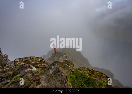 Le randonneur se trouve sur une pente rocheuse au sommet de Klakkur dans le brouillard, Klaksvík, îles Féroé. Banque D'Images