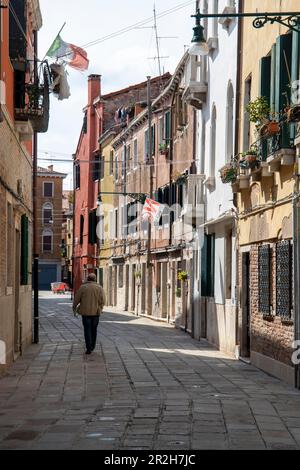 Un homme solitaire marche le long d'une rue étroite à l'ombre des maisons, Venise, Vénétie, Italie Banque D'Images