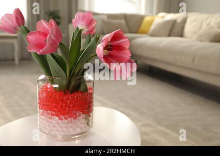 Différentes couleurs de remplissage et tulipes dans vase en verre sur table blanche à la maison, espace pour le texte. Perles d'eau Banque D'Images