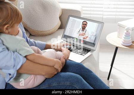 Mère et fille ayant une consultation en ligne avec le pédiatre via ordinateur portable sur le canapé à la maison Banque D'Images