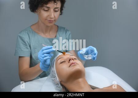 Cosmétologue appliquant un produit cosmétique pour l'exfoliant chimique sur le visage du client en salon Banque D'Images