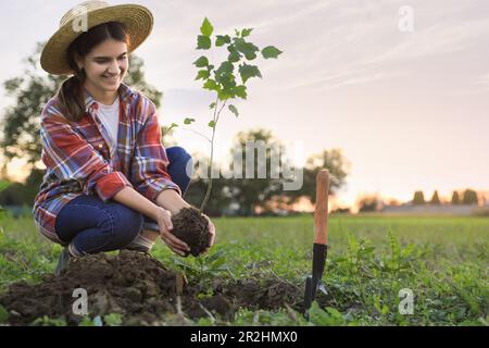 Jeune femme plantant un arbre à la campagne, espace pour le texte Banque D'Images