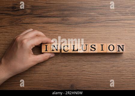 Femme faisant mot inclusion avec des cubes sur table en bois, gros plan avec vue de dessus Banque D'Images