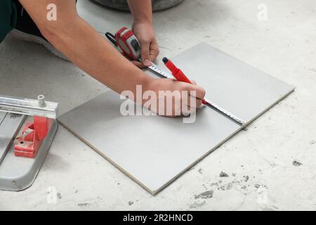 Employé mesurant et marquant les carreaux de céramique sur le sol, gros plan Banque D'Images