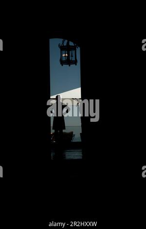 Élégant garçon en Silhouette debout avec ses mains sur les hanches sur une terrasse avec parasol et une lampe en Suisse. Banque D'Images