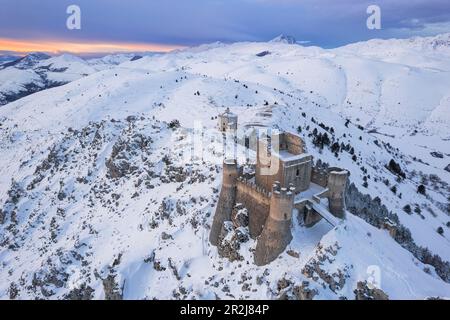 Vue aérienne en hiver du château de Rocca Calascio et de l'église Santa Maria della Pietà dans le paysage enneigé au crépuscule, Campo Imperatore Banque D'Images