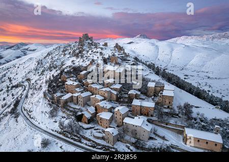 Vue aérienne en hiver du village médiéval enneigé de Rocca Calascio avec le château et les nuages roses au crépuscule Banque D'Images