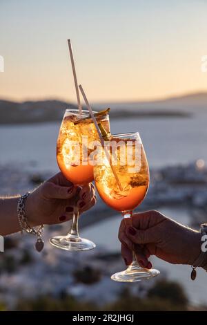 Mains de deux femmes en dégustant des cocktails Aperol Spritz au bar 180º Sunset sur la colline surplombant la ville et les îles, Mykonos, South Egée, Greec Banque D'Images