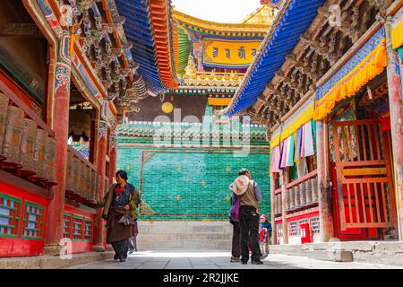 Les Tibétains marchent autour d'un temple richement décoré avec des roues de prière et un toit coloré et des ornements au monastère Kumbum Champa Ling, Xining, Chine Banque D'Images