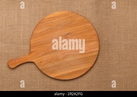 Table de service ronde en bois vide avec poignée sur la nappe en jute. Vue de dessus. Design plat minimaliste. Planche à découper avec espace de copie. T Banque D'Images