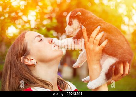 Jeune femme brune tenant et embrassant son petit chiot. Banque D'Images