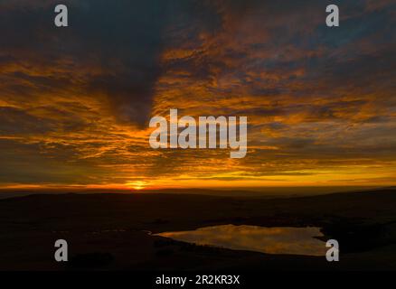 Une vue panoramique à couper le souffle de Malham Tarn au coucher du soleil, reflétant le ciel vibrant et les falaises calcaires dans ses eaux tranquilles. Banque D'Images