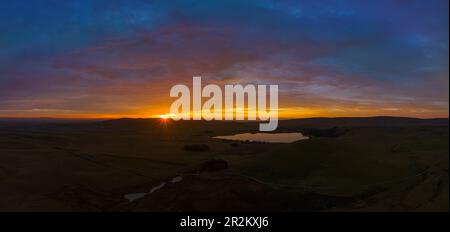 Une vue panoramique à couper le souffle de Malham Tarn au coucher du soleil, reflétant le ciel vibrant et les falaises calcaires dans ses eaux tranquilles. Banque D'Images