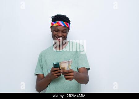 un jeune homme africain heureux tenant de l'argent et utilisant son téléphone Banque D'Images