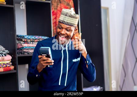 homme africain portant des vêtements africains vendant dans un marché de la mode en utilisant un point sur la machine de vente célébrant la transaction réussie. Mode de paiement, cashl Banque D'Images