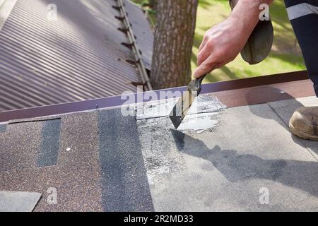 Réparation et construction. Les mains du travailleur appliquent du mastic sur le toit de la maison Banque D'Images