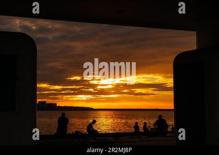 Les gens pêchent à partir d'un quai sur la rive du lac Érié de Cleveland et silhouettés par le soleil couchant Banque D'Images