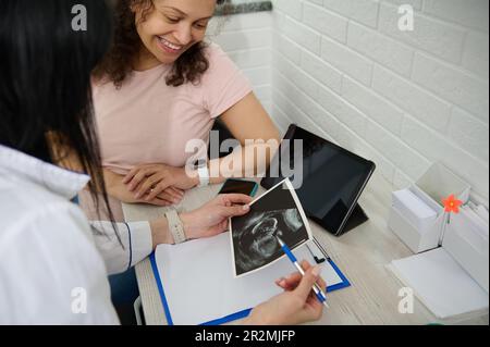 Femme médecin obstétricienne gynécologue expliquant à une femme enceinte heureuse l'échographie de son bébé dans l'utérus. Banque D'Images