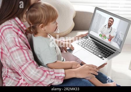 Mère et fille ayant une consultation en ligne avec le pédiatre via ordinateur portable sur le canapé à la maison Banque D'Images