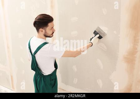 Travailleur dans un mur uniforme de plâtrage avec couteau à mastiquer à l'intérieur Banque D'Images