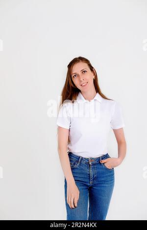 Une fille mignonne et souriante dans un T-shirt blanc sourit joyeusement et exprime des émotions positives sur un fond blanc. Banque D'Images