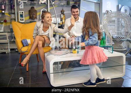 Jeune couple marié assis dans un magasin de lampe choisir une lampe avec leur petite fille, mère haute de cinq ans son enfant. Shopping, concept de style de vie. Banque D'Images